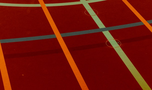 A sports court with intersecting lines in orange and blue, creating geometric patterns on a reddish-brown surface.